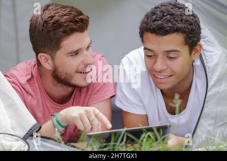two young men layed in tent looking at tablet Stock Photo