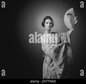 Young beautiful woman in traditional Japanese kimono dancing with a fan. Black and white. Copy space. Stock Photo