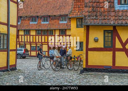 Group of kids on bikes near traditional half-timbered warehouses and old yellow houses in the old town of Kerteminde. Kerteminde, Denmark Stock Photo