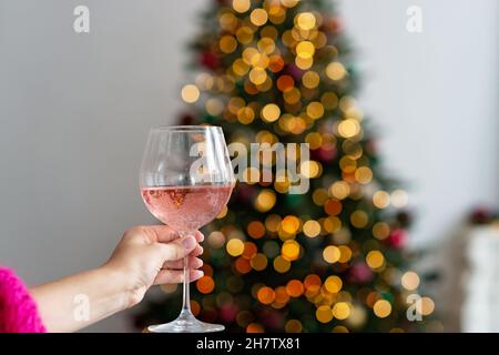 Glass of champagne rose in hand against the background of bokeh lights of the Christmas tree. Winter holiday. New year background. Soft selective focu Stock Photo