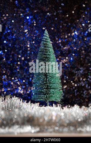 green glitter mini Christmas tree on blue sequin background with silver tinsel snow. Starry sky magic holiday forest lascape Stock Photo