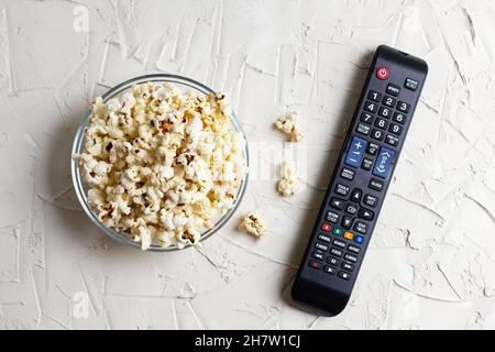 A transparent bowl of popcorn and TV remote on a white background. The concept of watching TV, film, TV series, sports, shows. Flat lay, top view. Stock Photo