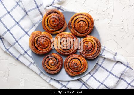 baked cinnamon buns on grey plate on light background with checkered napkin. Top view Stock Photo