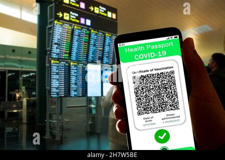 Spain. 24th Nov, 2021. In this illustrative photo a symbolic Covid certificate, also called covid passport, is seen on the screen of a mobile phone with an airport in the background in Barcelona, Spain on November 24, 2021. More and more countries are adopting the Covid19 vaccination passport for borders control, allowing only vaccinated people to travel. (Photo by Davide Bonaldo/Sipa USA) Credit: Sipa USA/Alamy Live News Stock Photo