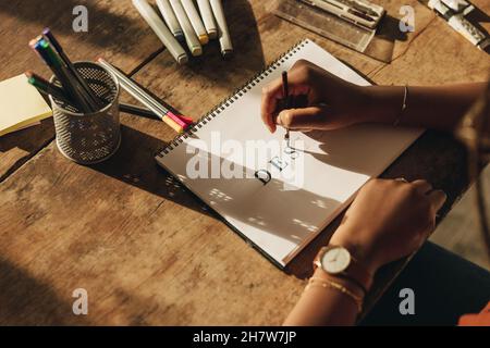 Woman drawing the word ''DESIGN'' while sitting at her workstation. High angle view of a young graphic designer working on a new project. Anonymous fe Stock Photo