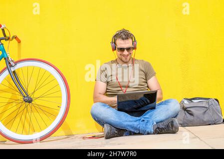 Young man working on laptop sitting on floor. Guy with computer reading news, surfing net or freelancing. Stock Photo