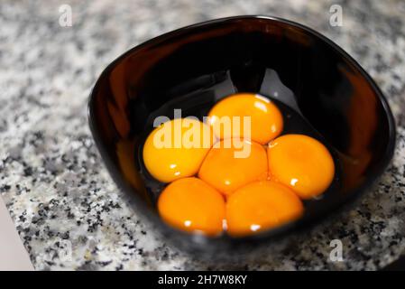 Egg yolks on a black bowl against a stone surface Stock Photo
