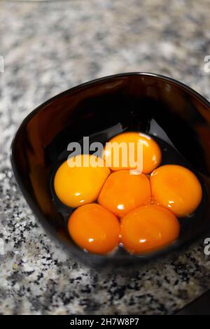 Egg yolks on a black bowl against a stone surface Stock Photo