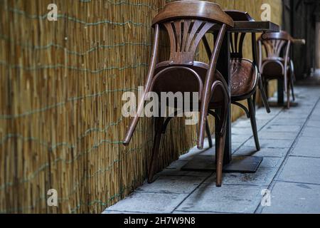 Brown wooden bistro chairs of a small restaurant stand empty leaning against tables in a narrow alley during the Corona Pandemic in Venice, Italy. Stock Photo