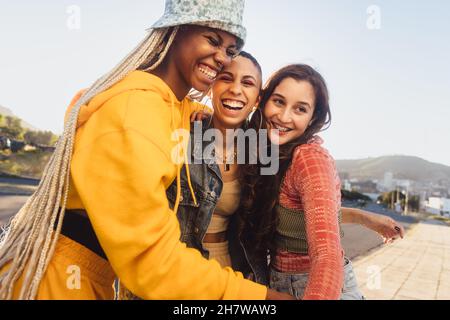 Young friends laughing together outdoors. Cheerful female youngsters having fun while standing together in the city. Group of generation z friends mak Stock Photo