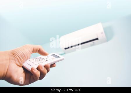 The air conditioner remote control is pressed by a human hand to regulate the temperature Stock Photo