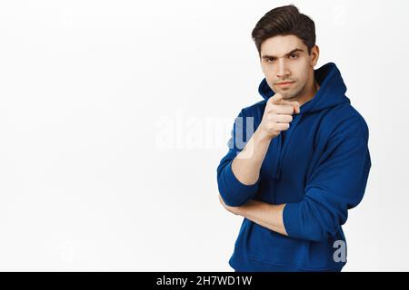 Suspicious man with frowned face, pointing finger at camera and looks serious at camera, stands over white background Stock Photo