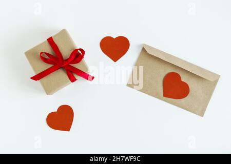 On a white background, a gift with a red ribbon, an envelope for a letter and hearts made of red cardboard. Stock Photo