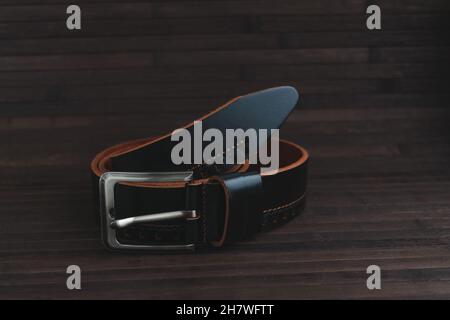 Men's leather trouser belt in black on a dark background of old wood. Stock Photo
