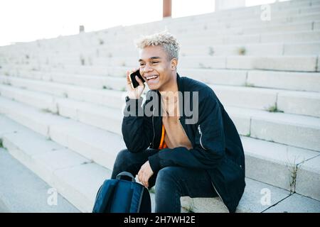 Young man sitting on stairs and having a conversation on a smartphone Stock Photo
