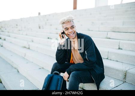 Young man sitting on stairs and having a conversation on a smartphone Stock Photo