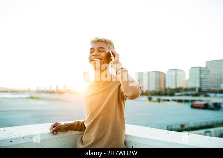 Young latin american male talking and smiling on a yellow smartphone during sunset, on a urban scape Stock Photo