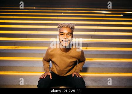 Young latin american male sitting on stairs and smiling at the camera, on the street Stock Photo