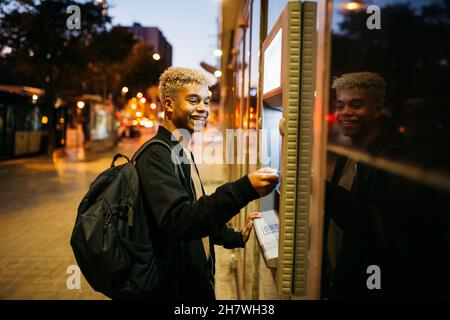 Young latin american male with a blue credit card  on a bank cashier, at dusk Stock Photo