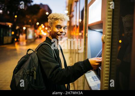 Young latin american male with a blue credit card  on a bank cashier, at dusk Stock Photo