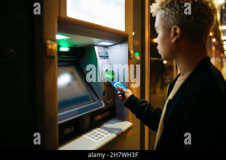 Young latin american male with a blue credit card  on a bank cashier, at dusk Stock Photo