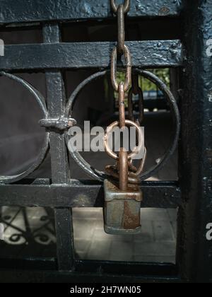A padlock on a metal chain hanging from an old wrought-iron gate. Elements of the architecture of the old city. Vertical photo. Stock Photo
