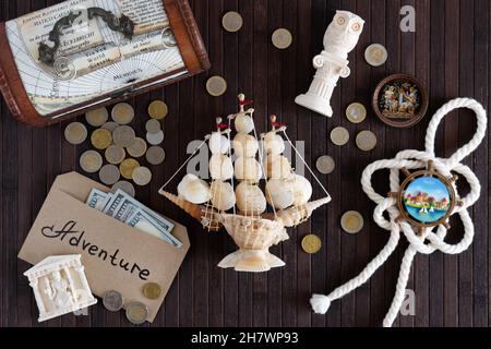 Vitebsk, Belarus - June 2021: On a dark wooden background, tourist magnets, coins, US banknotes , a knot, figurines, a chest, a ship made of shells. Stock Photo