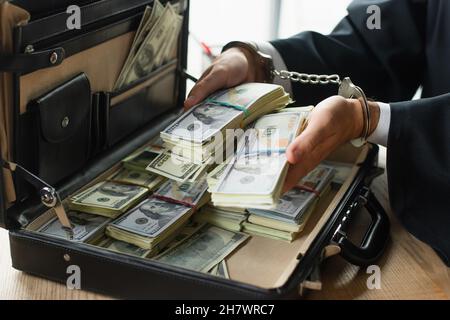 partial view of businessman in handcuffs holding dollars near briefcase, anti-corruption concept Stock Photo