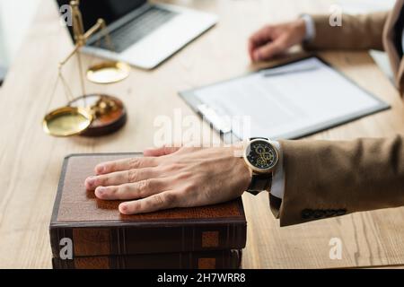 partial view of lawyer holding hand on codex book near blurred justice scales, anti-corruption concept Stock Photo