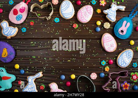 Cookie cutters, felt toys and Easter frosted cookies in shape of egg, chicken and rabbit on dark wooden background fat lay view. Stock Photo