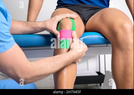 Physical therapist applying kinesio tape on male patient knee. Kinesiology, physical therapy, rehabilitation concept. close up. High quality photo Stock Photo
