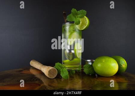 Glass of Mojito cocktail with mint and lime on a black board with fresh limes. Sparkling refreshing water. Place for text Stock Photo