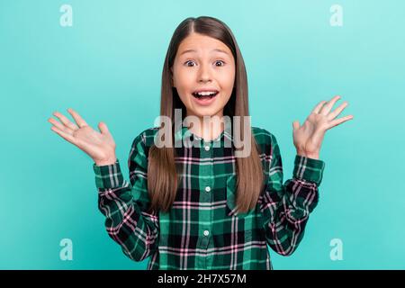 Photo of funky excited school girl dressed checkered clothes smiling rising arms isolated teal color background Stock Photo