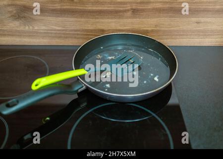 Dirty frying pan with plastic spatula on a induction glass hob on modern kitchen Stock Photo