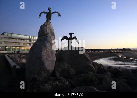 Seabird sculptures in front of the iconic art deco Midland Hotel (designed by Oliver Hill) at dusk in the autumn from the beach, Morecambe, Lancashire Stock Photo