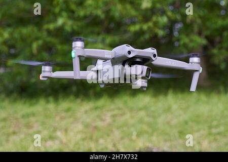 Nürtingen, Germany - June 26, 2021: Gray Dji air 2s drone hovers over the green meadow. Tree in the background. Stock Photo