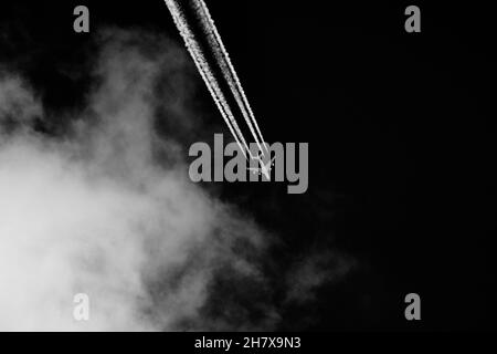 Airplane leaves contrails in the sky with clouds on black background. Stock Photo