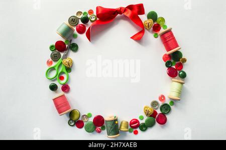 Christmas wreath made of buttons, threads, pins, scissors, thimble red, green and gold color. White background. Copy space. Stock Photo