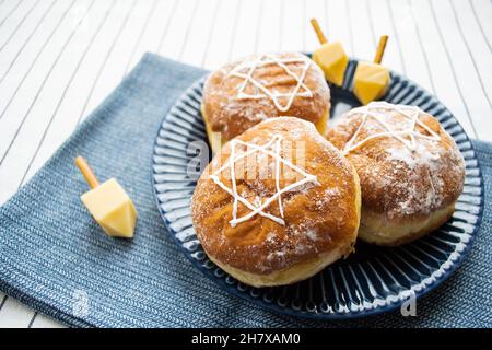 Happy Hanukkah. A traditional treat of doughnuts with David star and dreidel made from cheese and biscuit sticks. Copy space. Stock Photo