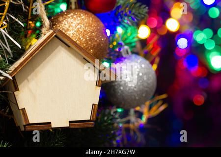 Christmas toy wooden house on the Christmas tree on the colorful lighting background. Beautiful Christmas decorations. Cool bright New Year's toys Stock Photo