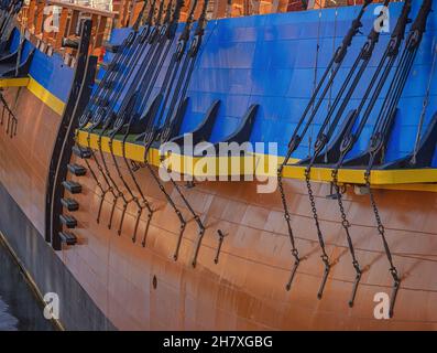 A side view of the replica of an historic ship. Rigging lines are attached to platforms and half fast by chains. A canon protrudes over the side. Stock Photo