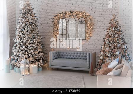 classic apartment with a white sofa decorated with wood, large windows and mirrors. Christmas evening by the light of garlands. Classic luxury apartme Stock Photo
