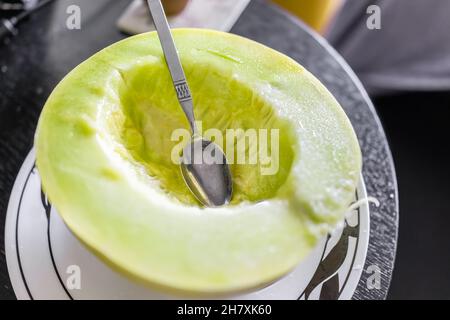 Closeup of one vibrant colorful yellow green honey honeydew melon half cut with spoon eating on plate macro Stock Photo