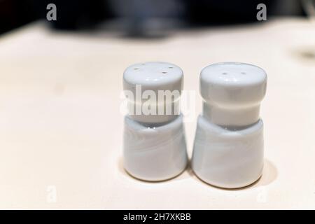 Macro closeup of white ceramic salt and pepper shakers in bottles on table in restaurant cafe Stock Photo