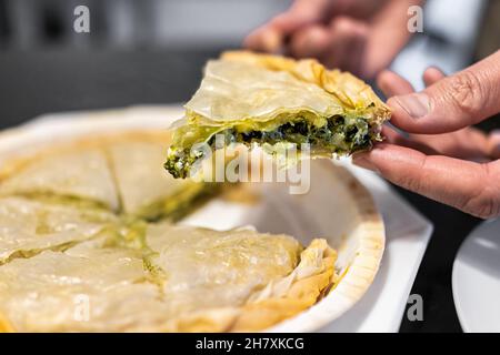 Person hand taking slice of cooked baked filo dough Spanakopita from whole pie traditional greek food made with spinach and cheese macro closeup Stock Photo