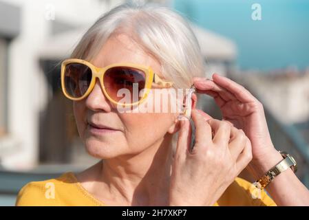 Senior woman puts on the hearing aid. Deafness, senior health care concept Stock Photo