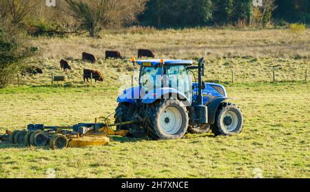 Large blue New Holland T7 210 tractor with a trailed grass topper Stock Photo