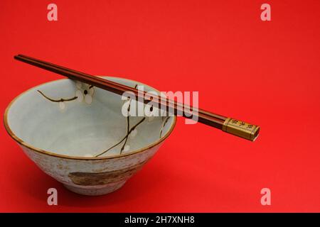 Vintage blue Rice bowl with sakura flowers and traditional bamboo chopsticks on bright red background. Stock Photo