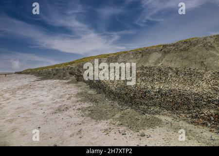 Eroded beach ridge formed by storm and waves, making a thick bottom layer with sea shells visible Stock Photo