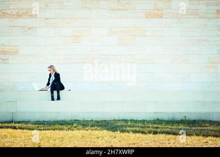 Young woman sitting on steps and working on notebook computer, business concept Stock Photo